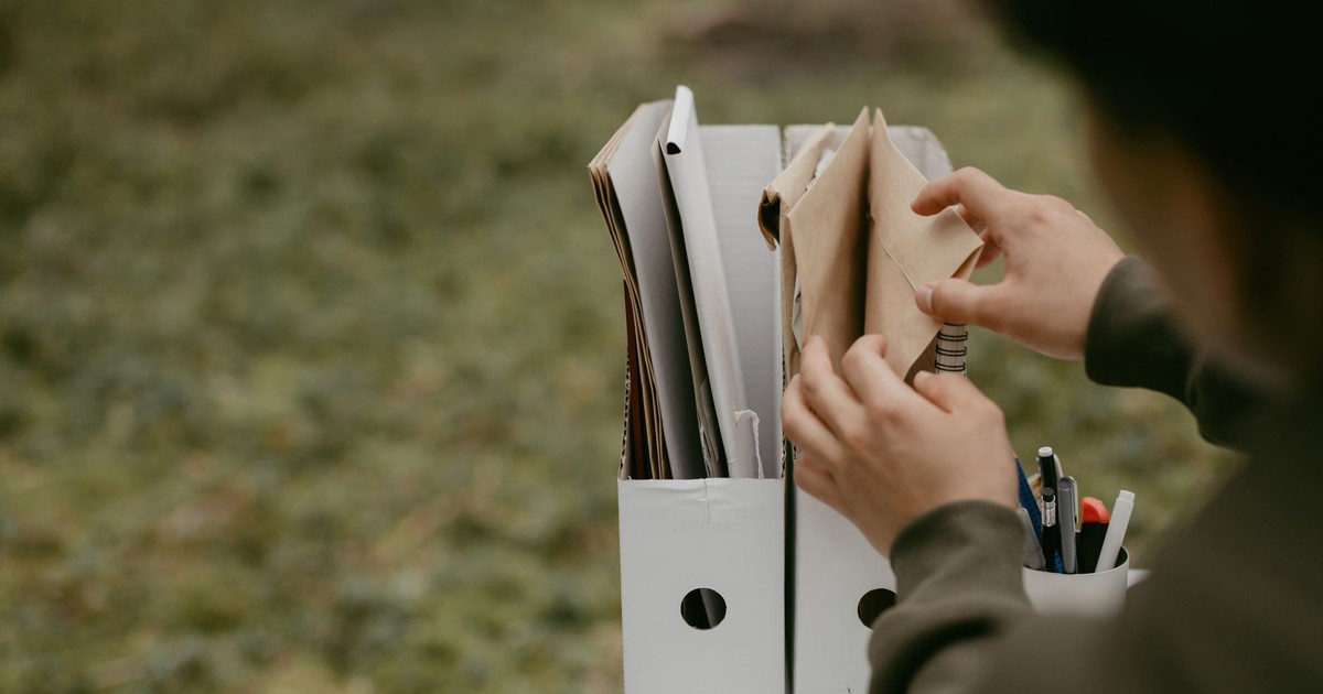 Person sorting documents in folders outdoors, hands visible, neutral tone.