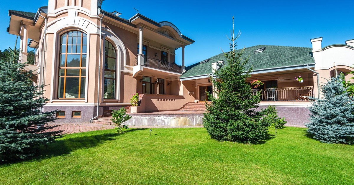 Modern luxury villa with large windows, surrounded by lush green lawn and trees.