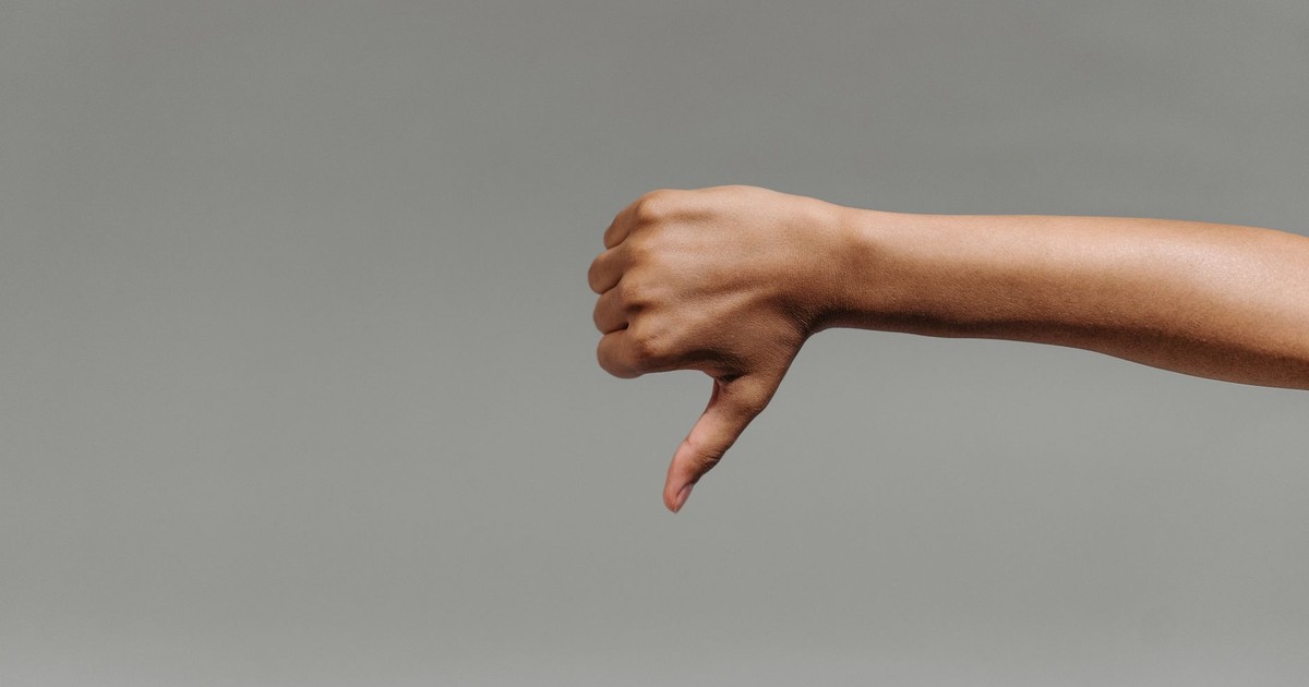 Close-up of a person's hand giving a thumbs down gesture against a gray background.