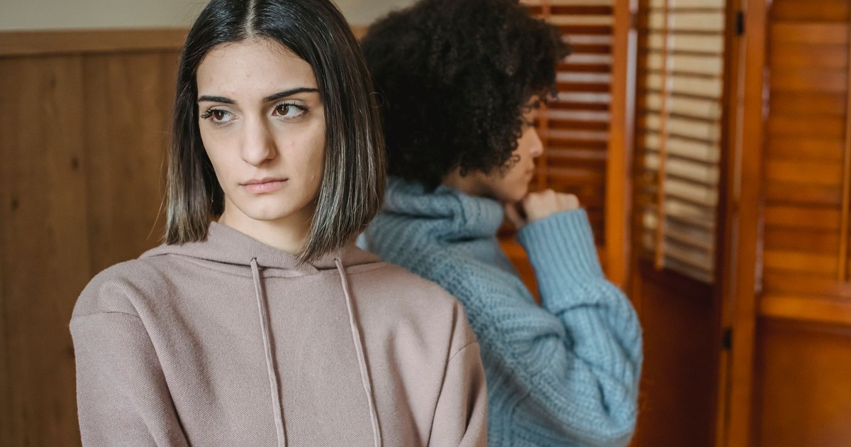 Upset multiracial women in casual wear standing in light room near wall with wooden folding screen while having conflict at home