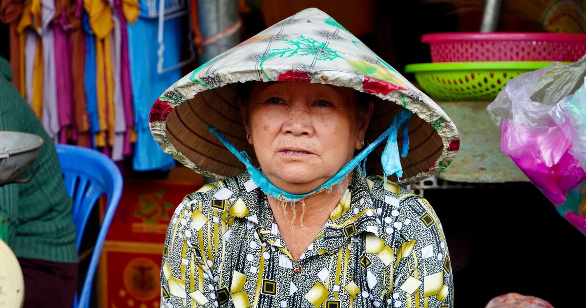 Elderly Vietnamese woman wearing a conical hat at a bustling market.