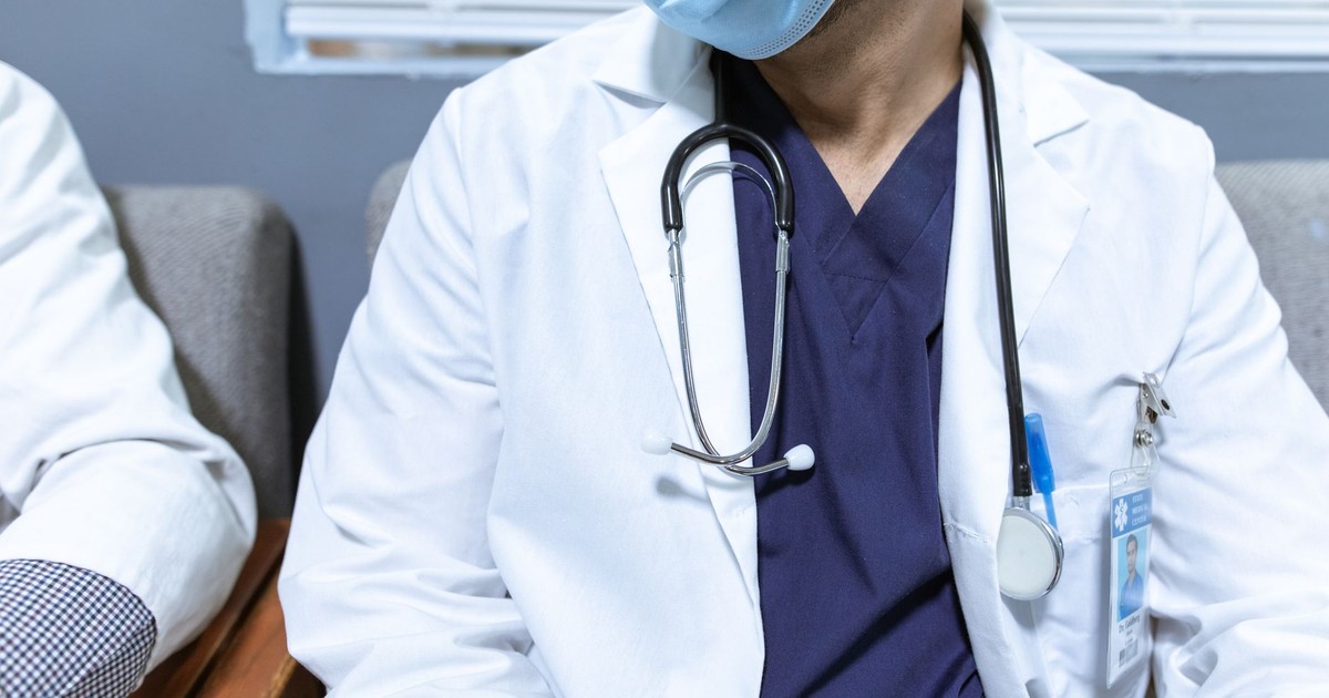 Close-up of a healthcare worker wearing a mask and stethoscope, seated indoors.
