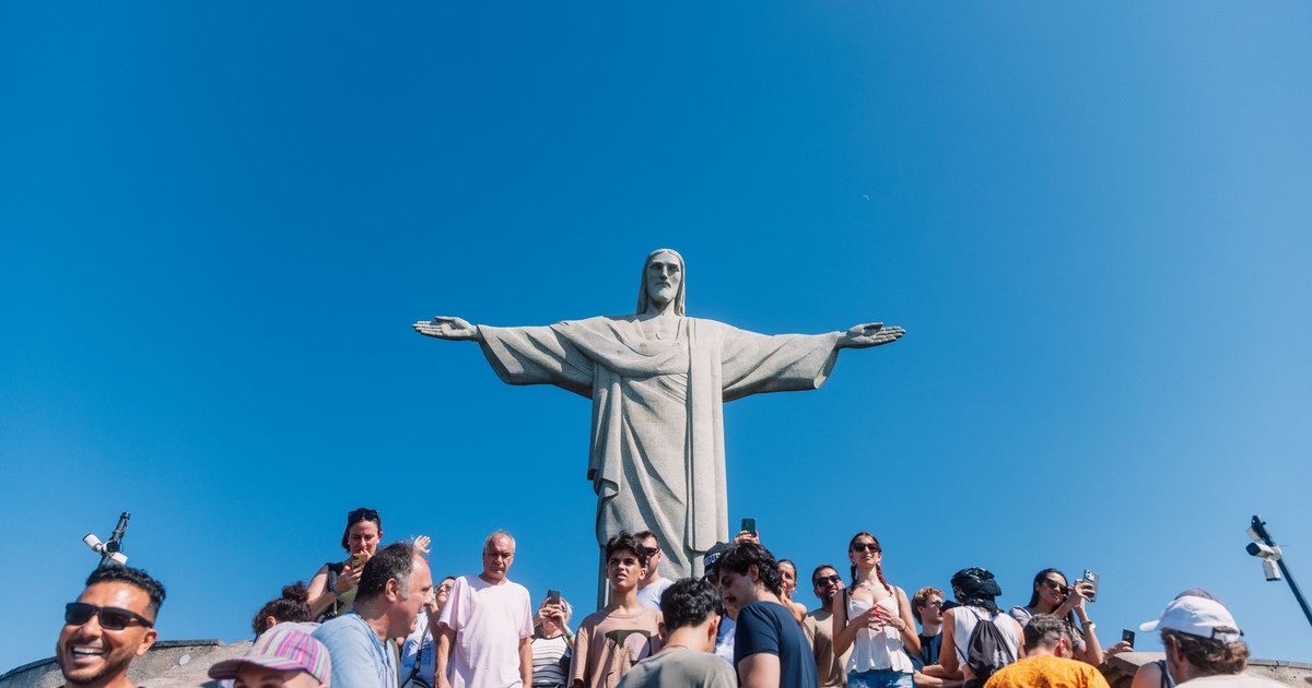 Tourists gather at the iconic Christ the Redeemer statue under clear blue skies in Rio de Janeiro, Brazil.