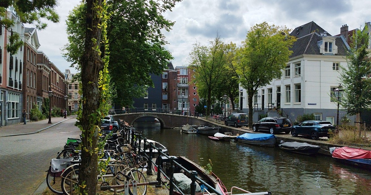 A scenic Amsterdam canal with parked bicycles and covered boats under a cloudy sky.