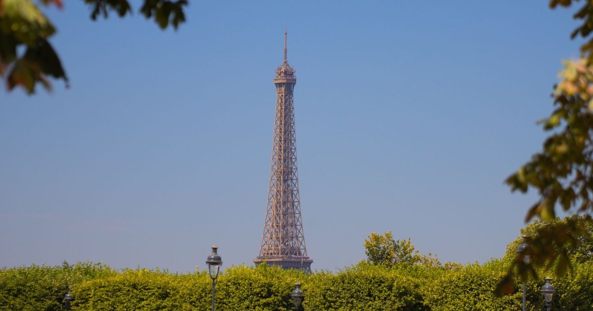 Scenic view of the Eiffel Tower framed by lush green trees against a clear blue sky in Paris, France.
