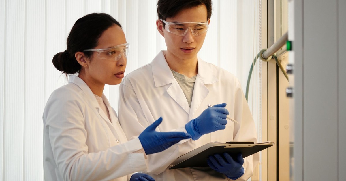 Researchers discussing data in a laboratory setting, wearing safety gear and blue gloves.