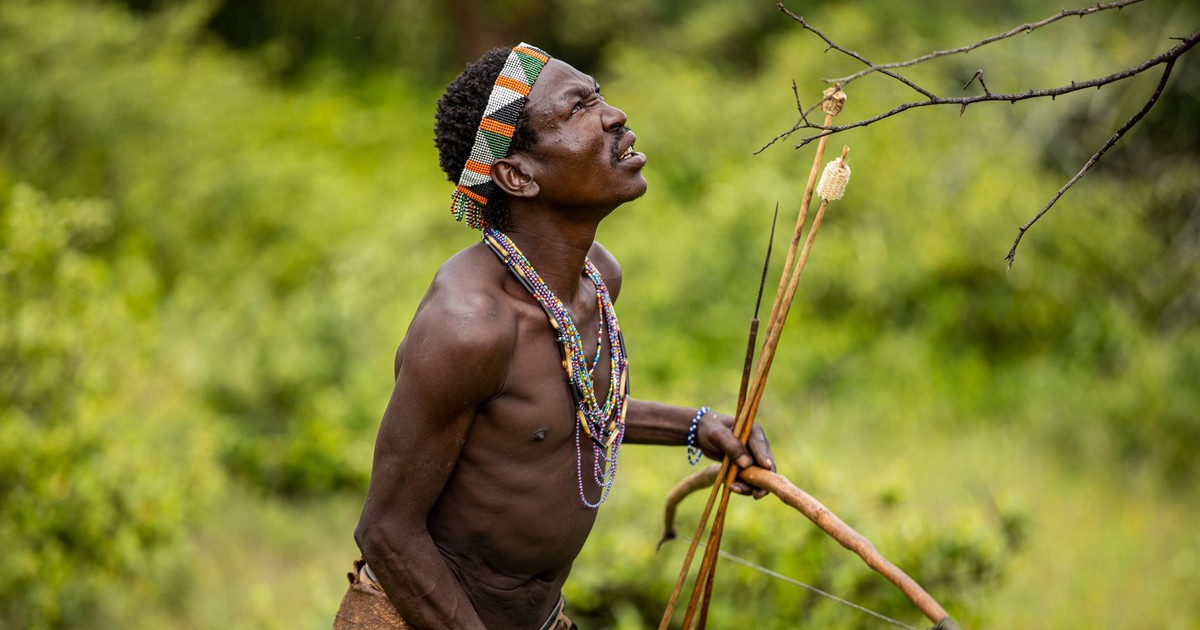 Portrait of a traditional hunter with a bow, set in lush greenery, capturing cultural heritage.