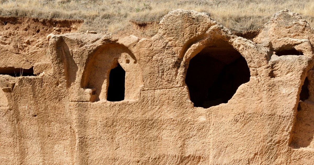 Explore an ancient cave dwelling with arched openings carved into rocky terrain, showcasing historical architecture.