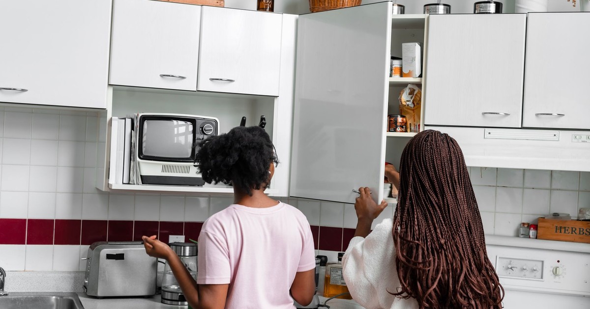 Two women organizing kitchen cabinets in a modern home kitchen with appliances and fixtures.