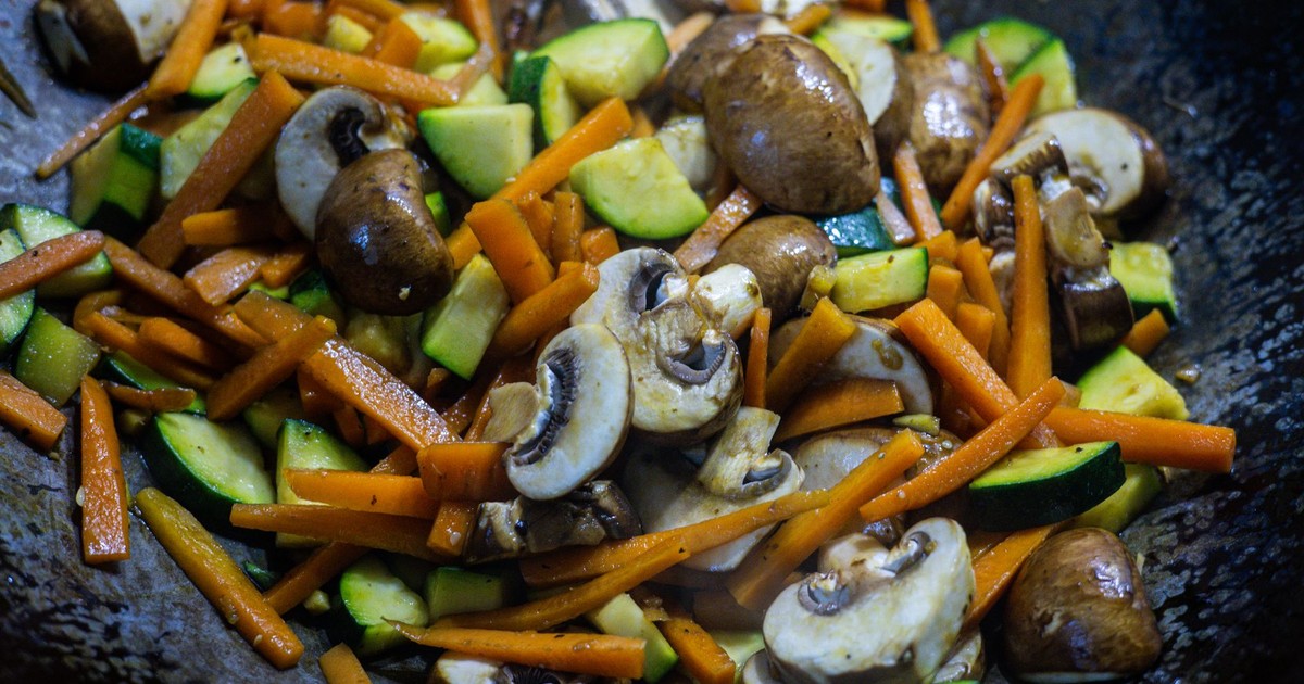 Close-up of vibrant stir-fried vegetables including mushrooms, carrots, and zucchini in a wok.