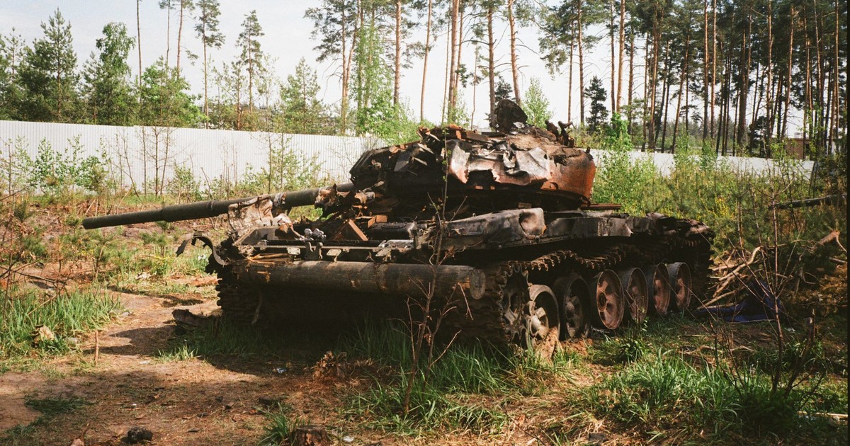 A destroyed military tank lies abandoned in a forest near Bucha, Ukraine amidst war-torn surroundings.