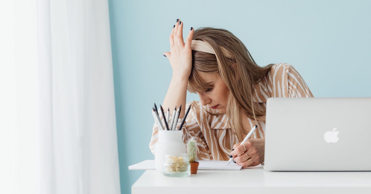 Caucasian woman with hand on head looking stressed while working on laptop in home office.