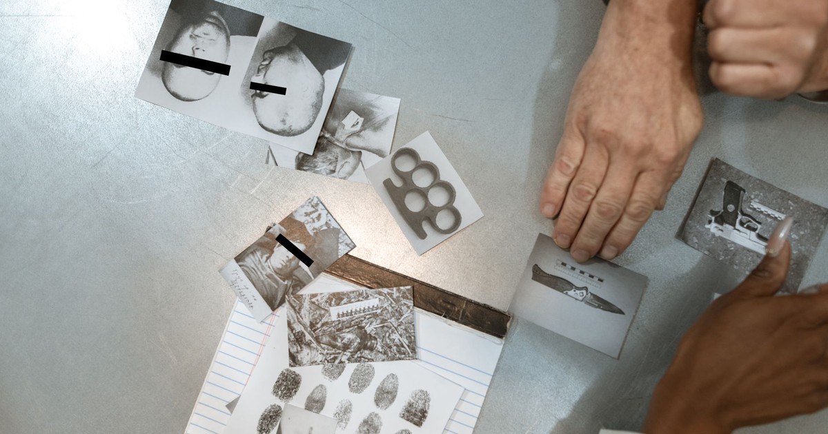 Hands of a handcuffed man examining criminal evidence with an officer.