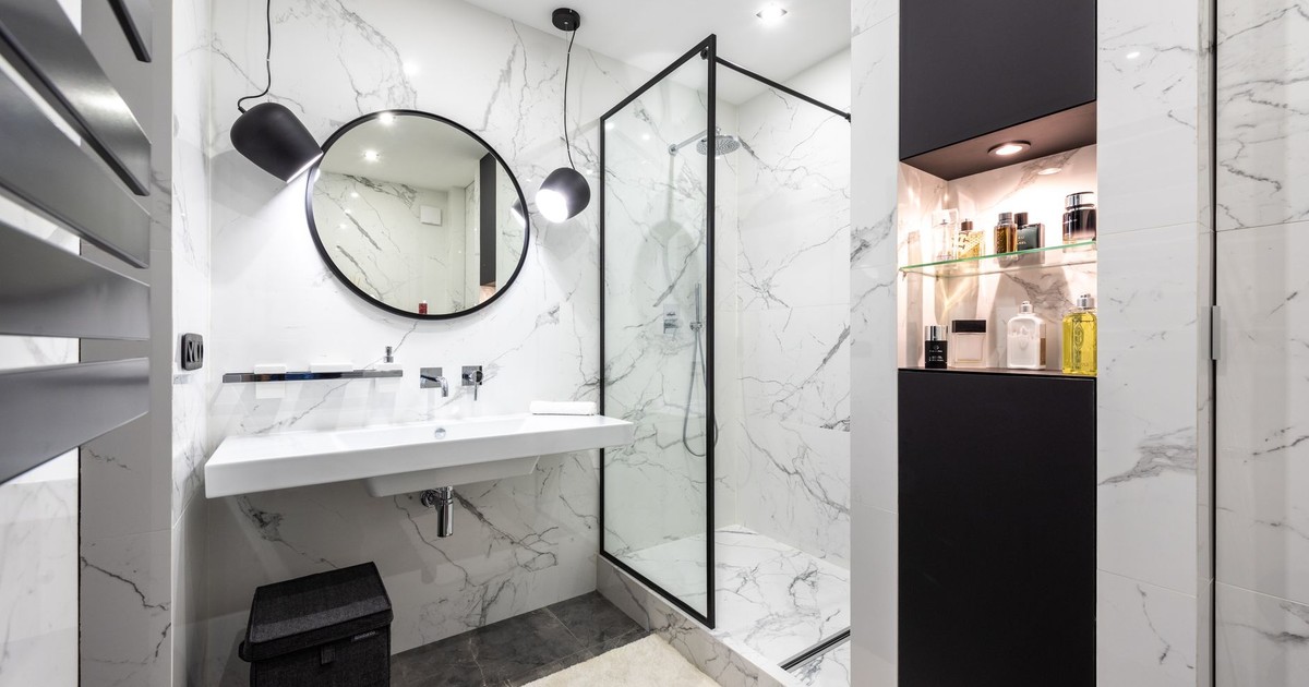 Shower room against washbasin and mirror between shiny lights in bathroom with assorted perfume in bottles on shelves