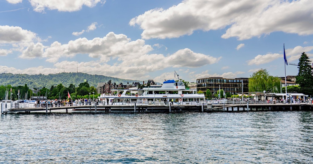 A bustling waterfront with a ferry docked against a backdrop of hills under a cloudy sky.