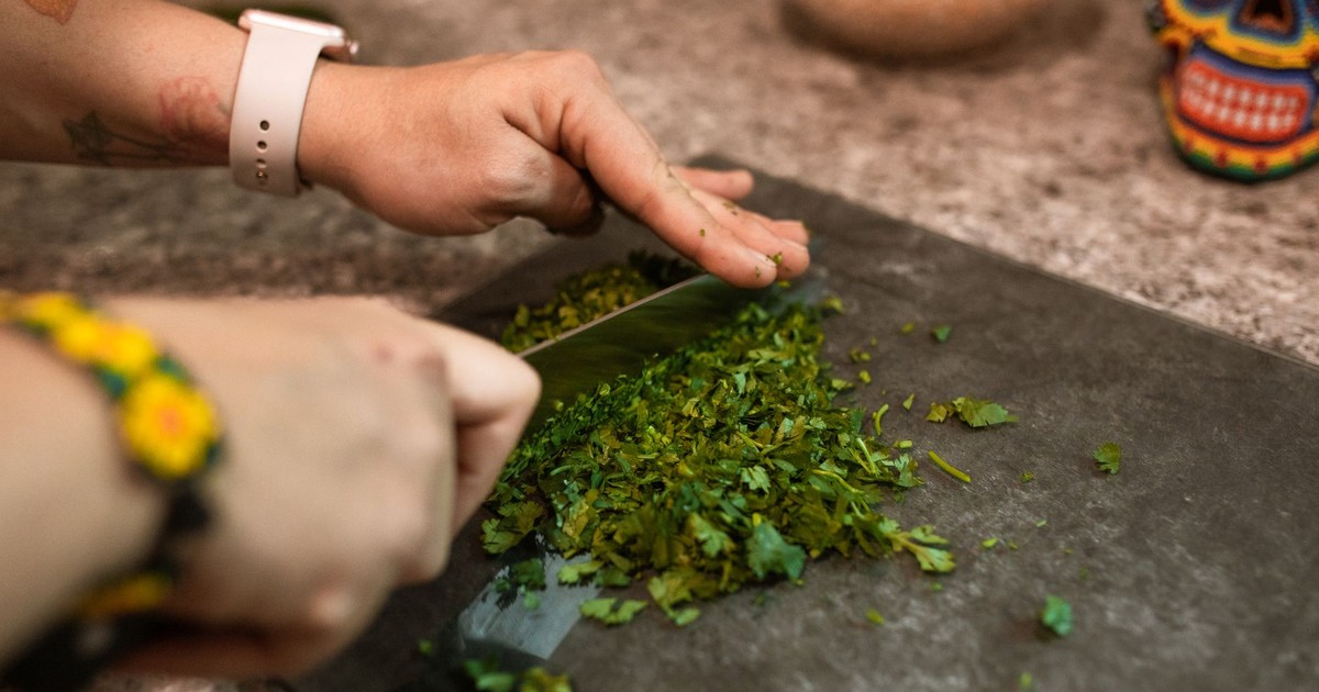Hands chopping fresh herbs on a cutting board, capturing food preparation process.