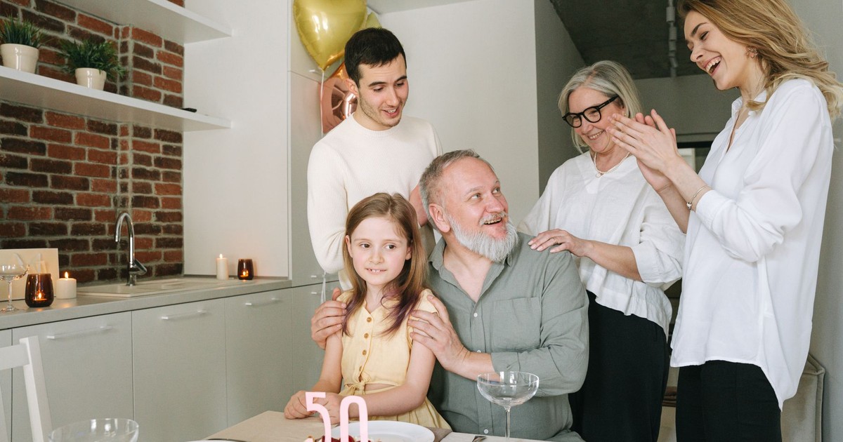 A joyful family celebration indoors with a birthday cake and balloons marking the 50th milestone.