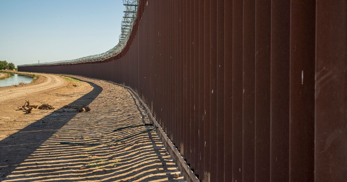Long view of a steel border wall under clear skies, emphasizing solitude and division.