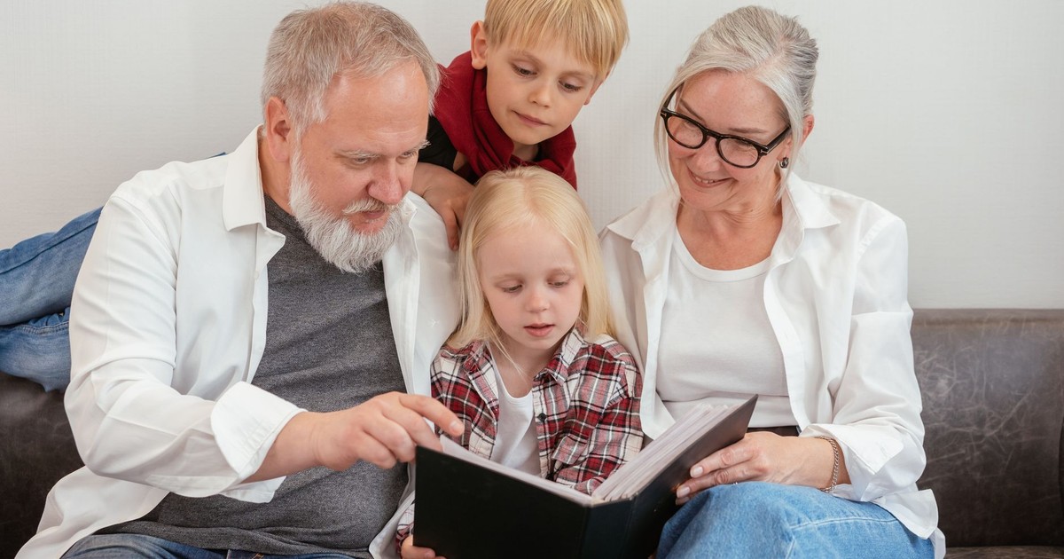 Grandparents and grandchildren reading a photo album on the couch, embracing family bonds and love.