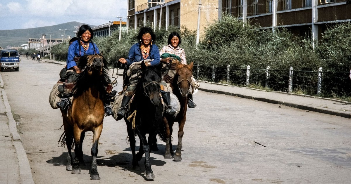 Three nomadic riders on horseback navigate a Chinese urban street, blending tradition with modernity.