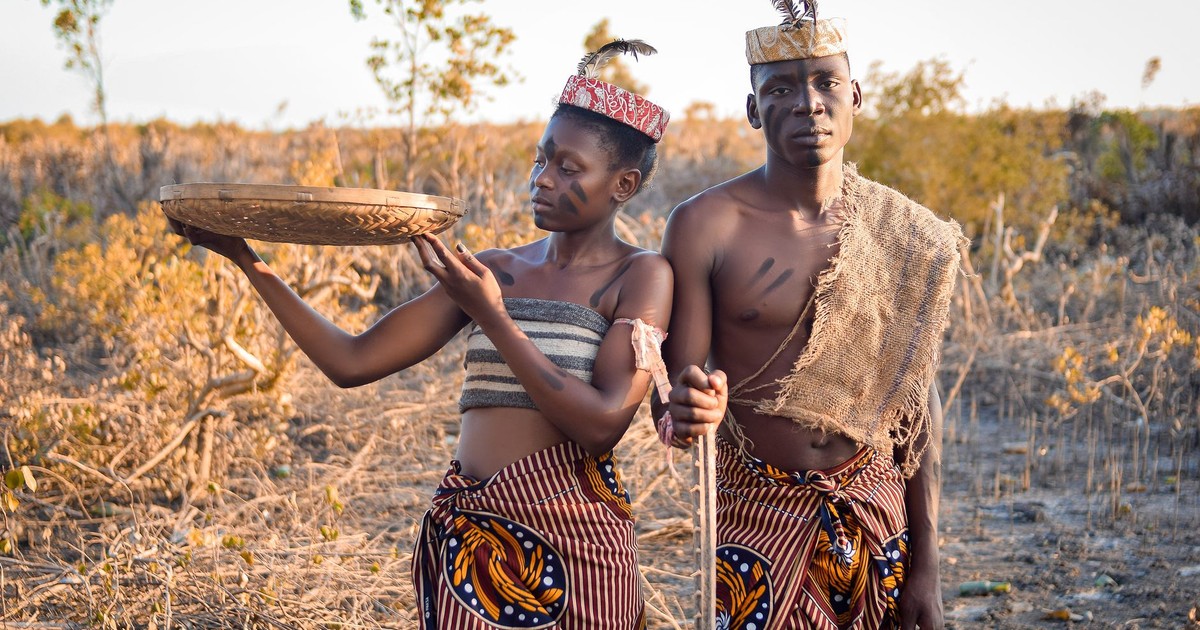 Two adults in traditional African attire stand together outdoors, embracing cultural heritage.