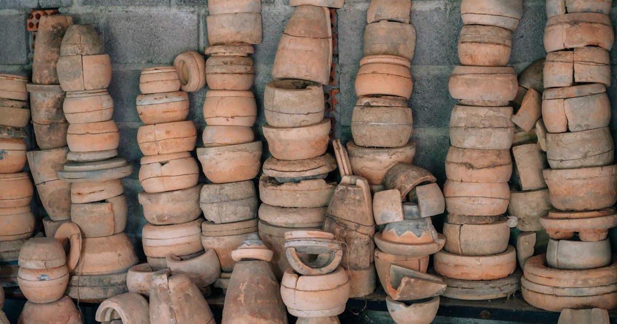 An array of handmade clay pottery pieces stacked against a cement wall, showcasing rustic craft.