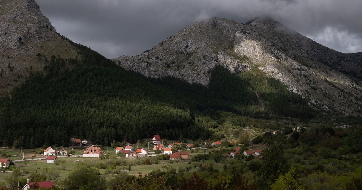 Picturesque village set against Montenegrin mountains and dramatic cloudy sky.
