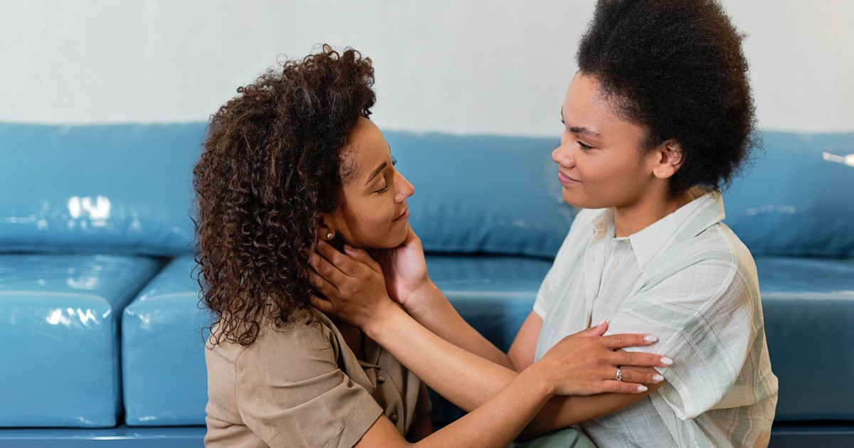 Two women embracing lovingly on a blue sofa, showcasing affection and connection.