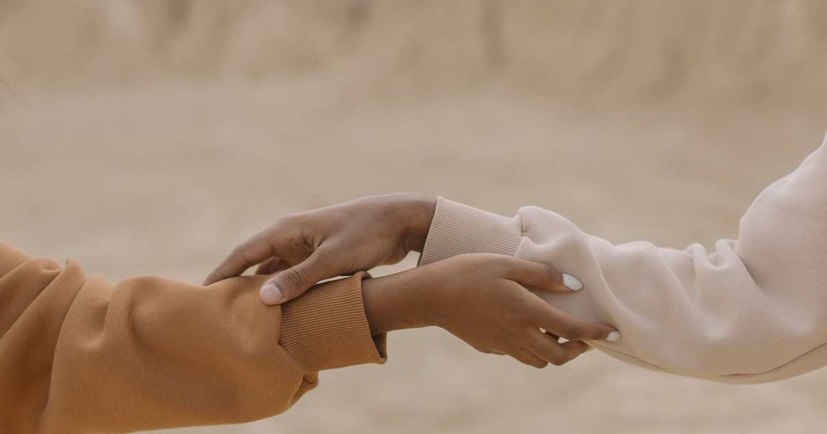 Close-up view of two hands reaching and holding each other against a muted background, symbolizing connection.