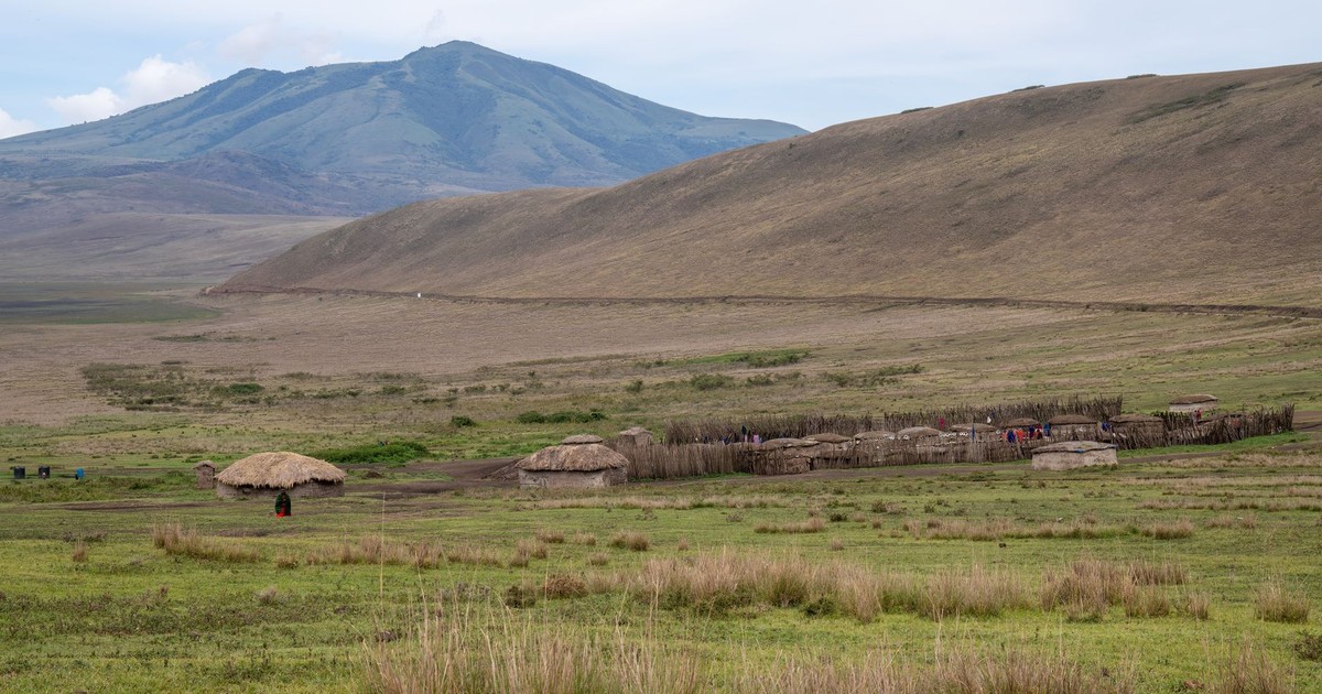 Scenic view of a traditional village with huts surrounded by vast grasslands and hills.