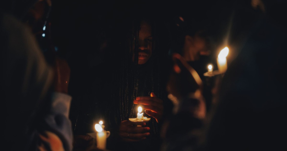 A solemn candlelit vigil at night with people holding lighted candles.