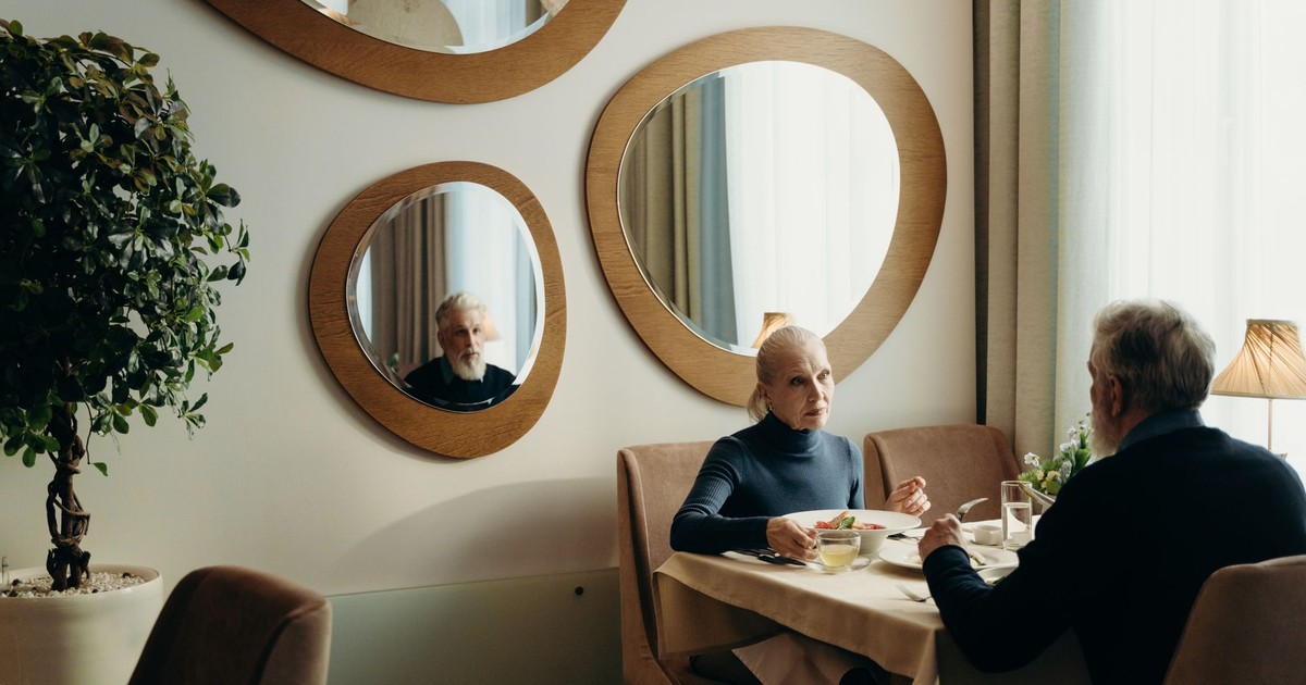 An elderly couple enjoys a meal in a cozy restaurant with warm lighting and elegant decor.