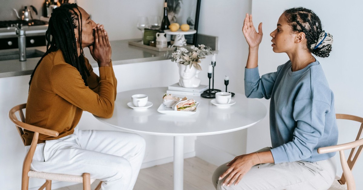 Side view of young African American female sitting at table while arguing with male in casual clothes
