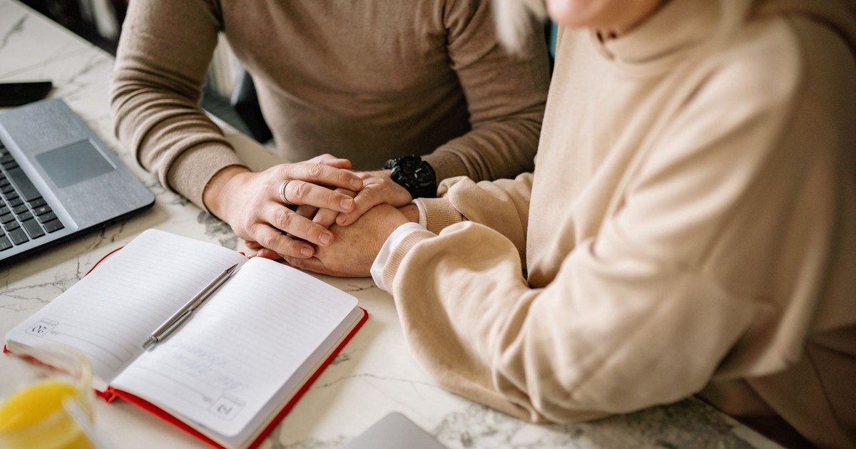 Close-up of a couple holding hands over an open planner at a marble table, symbolizing love and planning.