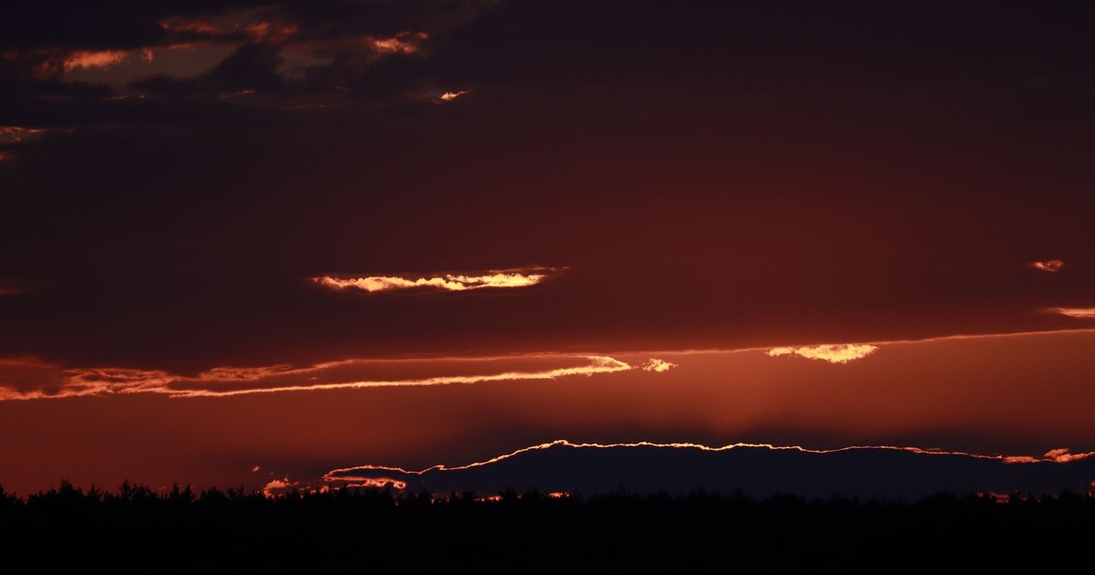A breathtaking sunset casting silhouettes over distant trees, creating a dramatic and serene scene.