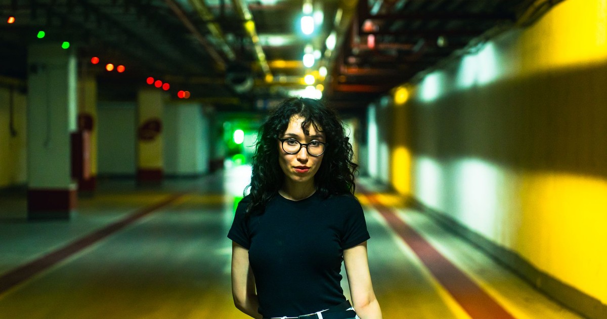 A fashionable woman stands confidently in a brightly lit urban tunnel.