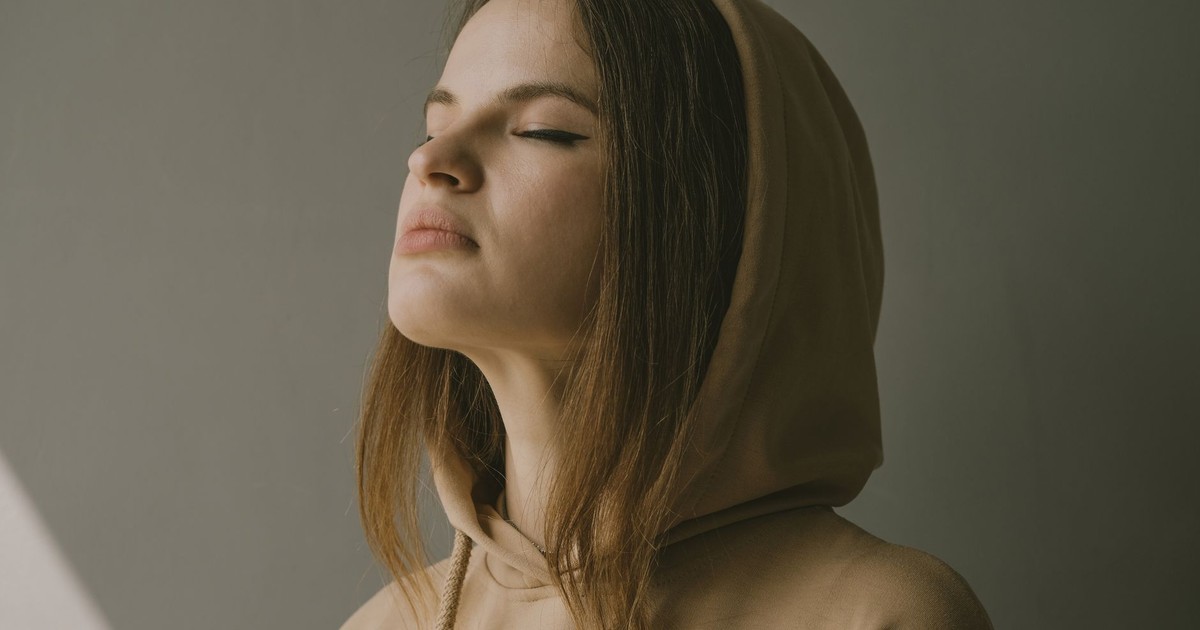 Portrait of a young woman in deep thought, wearing a beige hoodie indoors.