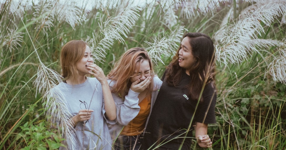 Three women enjoying a lighthearted moment amidst tall pampas grass in a natural outdoor setting.